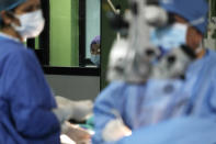 A Nepalese patient, center watches Dr. Sanduk Ruit perform cataract surgery as she waits her turn at the Tilganga Eye Center in Kathmandu, Nepal, March 26, 2021. Nepal’s “God of Sight” eye doctor renowned for his innovative and inexpensive cataract surgery for the poor is taking his work beyond the Himalayan mountains to other parts of the world so there is no more unnecessary blindness in the world. Ruit, who has won many awards for his work and performed some 130,000 cataract surgery in the past three decades, is aiming to expand his work beyond the borders of his home country and the region to go globally. (AP Photo/Niranjan Shrestha)