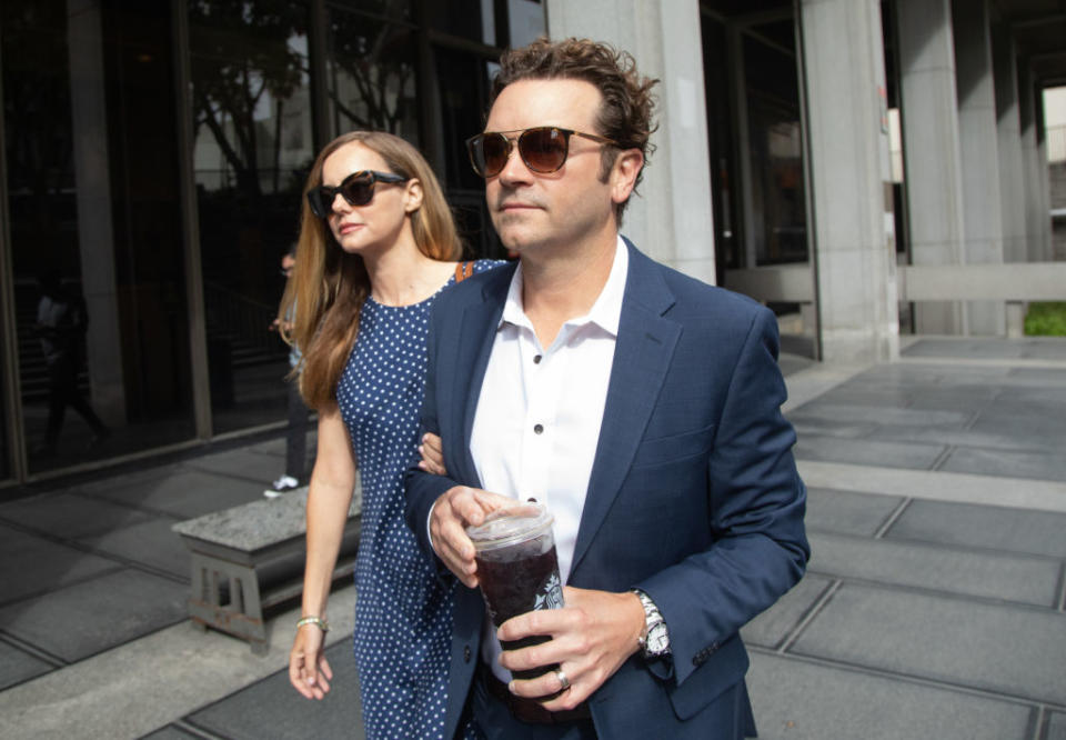 Masterson in a suit with a woman in a polka dot dress walking outdoors. He holds a drink