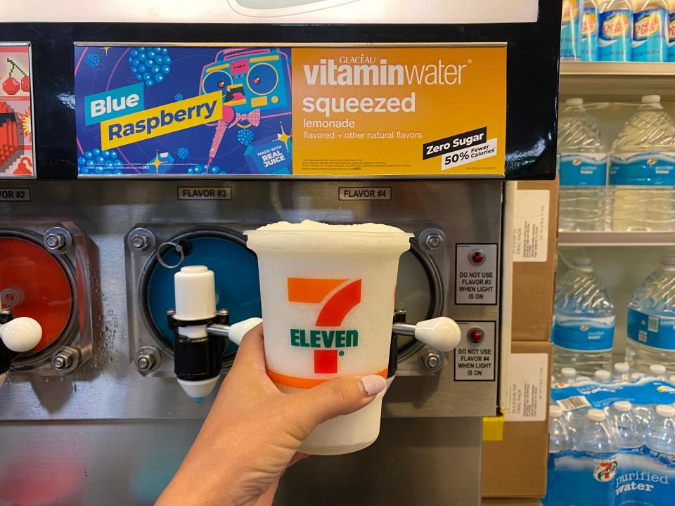 A hand filling up a large 7/11 cup with vitamin water squeezed lemonade slurpee