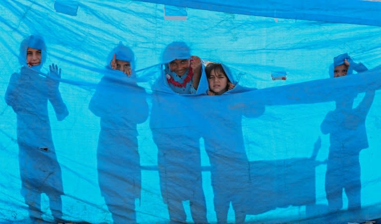 Iraqi children peer through a tarpaulin as they collect water from a tank at the Al-Khazir camp for civilians displaced by the fight for Mosul