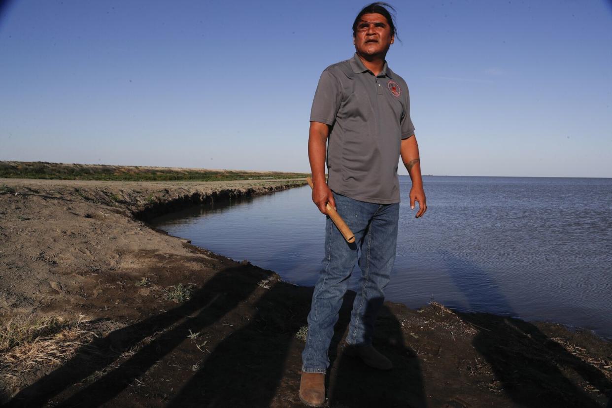 A man holding a traditional clapper stick stands at the edge of Tulare Lake.