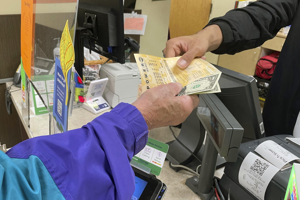 From behind the lottery counter at a Pick 'n Save store in Madison, Wis., Djuan Davis hands Powerball tickets to Arpad Jakab, a retired utility worker who said it's his first time buying them. The Powerball jackpot recently reached a record high of $1.6 billion. (AP Photo/Harm Venhuizen)