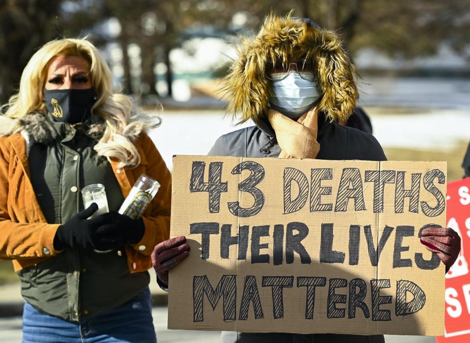 A woman and a man in face masks and winter coats, holding a cardboard sign reading '43 dead their lives mattered'