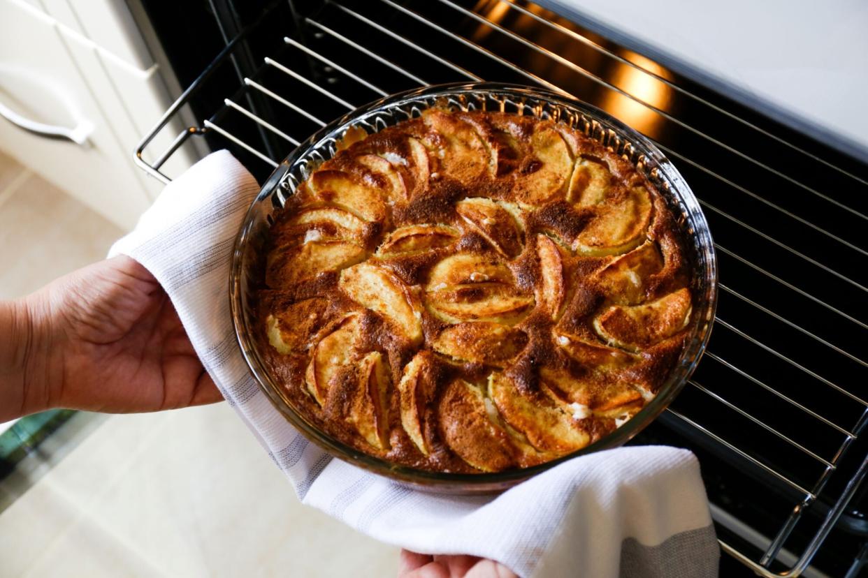 Fresh out of oven apple tart with cinnamon. Cropped shot of woman's hands taking out the pie baked to golden crust from the electric stove.