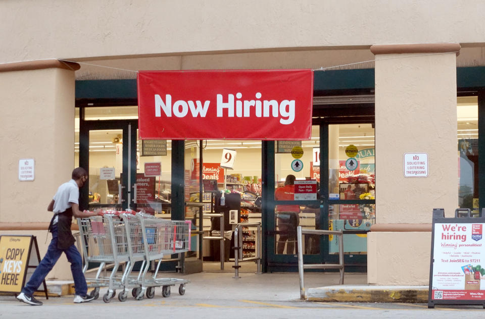  A Now Hiring sign hangs near the entrance to a Winn-Dixie Supermarket in Hallandale, Florida