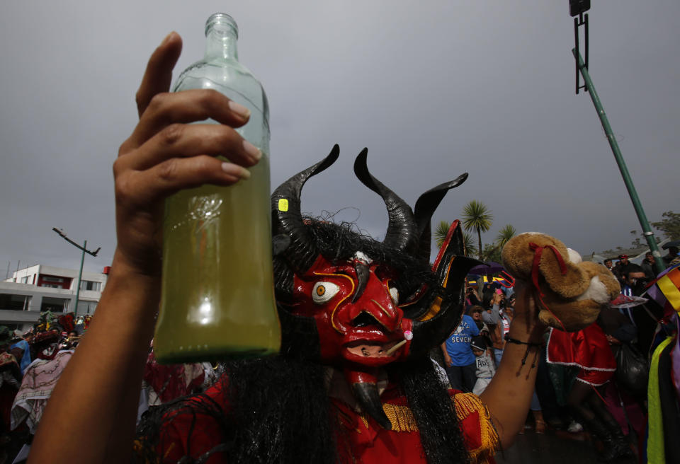A man with a devil's mask and a bottle of moonshine dances in La Diablada in Pillaro, Ecuador, Monday, Jan. 6, 2014, to celebrate the end of the year and the start of the new one. The town of Pillaro kicks off the Diablada with neighborhoods competing to bring in as many people as possible dressed as different characters. Originally the devil costume was used to open up space to allow other participants to dance, but over the years the character gained popularity and became the soul of the feast. (AP Photo/Dolores Ochoa)