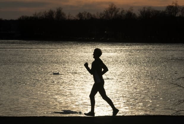 A runner is silhouetted as they take a path along the Ottawa River on March 30, 2021.