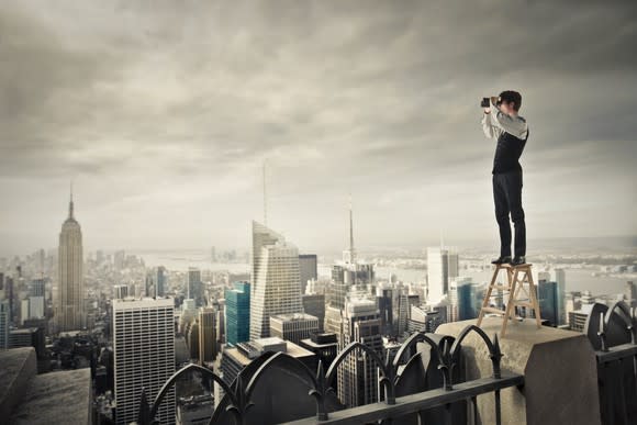 Man standing on a stool atop a building overlooking the city.