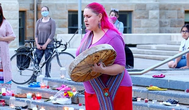 Chantal Chagnon drums at a vigil in Calgary for the children of Kamloops Indian Residential School on Tkâemlups te SecwÃ©pemc First Nation. Shoes, representing the 215 childrens' bodies found buried at the former school site in B.C. this week, were laid on the steps of city hall.