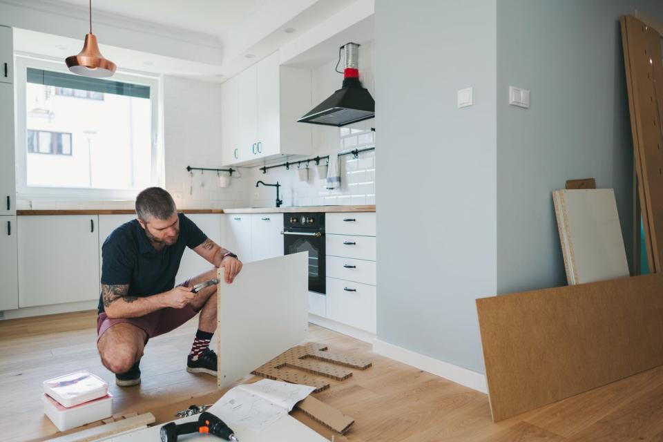 A squatting man works on a kitchen remodel.