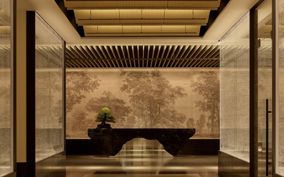 The front desk at Janu Tokyo is hewn from black rock and backed by a wall textile of tree etchings