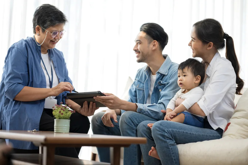 Home and Investment Loans, and Family First Credit. Asian female financial advisor or real estate agent and clients talking and discussing financial plan over a tablet computer at a new home for sale.