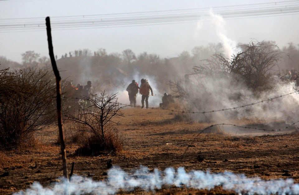 Striking mineworkers are caught in teargas as police open fire on striking miners at the Lonmin Platinum Mine near Rustenburg, South Africa, Thursday, Aug. 16, 2012. An unknown number of people have been killed and injured. Police moved in on workers who gathered on a rocky outcropping near the Lonmin late afternoon, firing unknown ammunition and teargas. (AP Photo) SOUTH AFRICA OUT