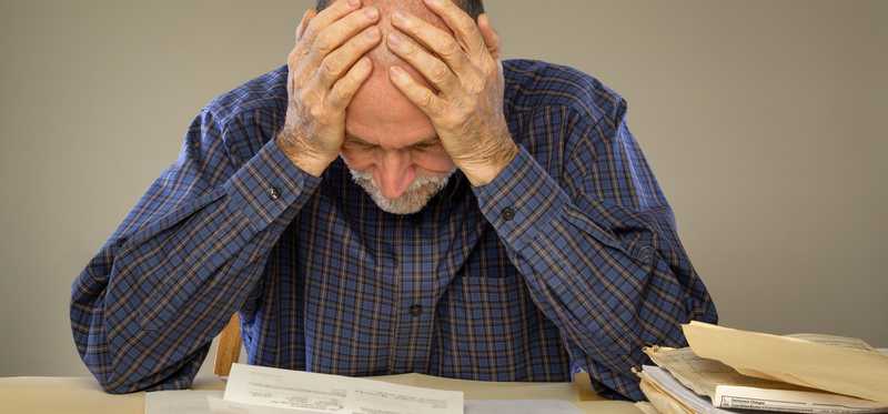 Older gentleman hunched over with his hands on his head.