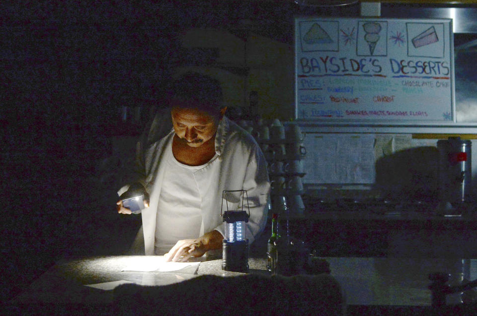 FILE - In this Wednesday, Oct. 9, 2019, file photo, Carlos Lama of Bayside Cafe, which was among businesses to lose power due to Pacific Gas & Electric Corp's public safety power shutoff, uses an LED lamp and light from his phone at the counter of the restaurant in Sausalito, Calif. California's largest utility pledged to improve communications but reminded state regulators that its "difficult decision" to pre-emptively shut off power to more than 2 million people last week may have prevented deadly wildfires. (Alan Dep/Marin Independent Journal via AP, File)