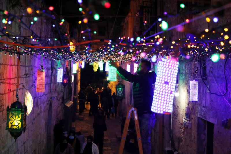Un hombre coloca luces decorativas en un pasaje en la Ciudad Vieja de Jerusalén como parte de los preparativos para el mes sagrado musulmán del Ramadán, en medio de una flexibilización de las restricciones por la pandemia de coronavirus