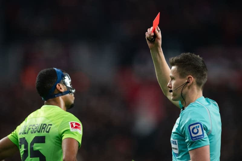 Referee Daniel Siebert (R) shows Wolfsburg's Moritz Jenz the yellow-red card during the German Bundesliga soccer match between Bayer Leverkusen and VfL Wolfsburg at BayArena. Marius Becker/dpa