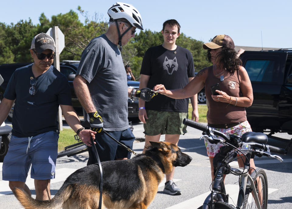 President Joe Biden stands with his dog Commander as he talks with a woman at Gordons Pond in Rehoboth Beach, Del., Saturday, June 18, 2022. Earlier Biden fell as he tried get off his bike to greet a crowd along the trail. (AP Photo/Manuel Balce Ceneta)