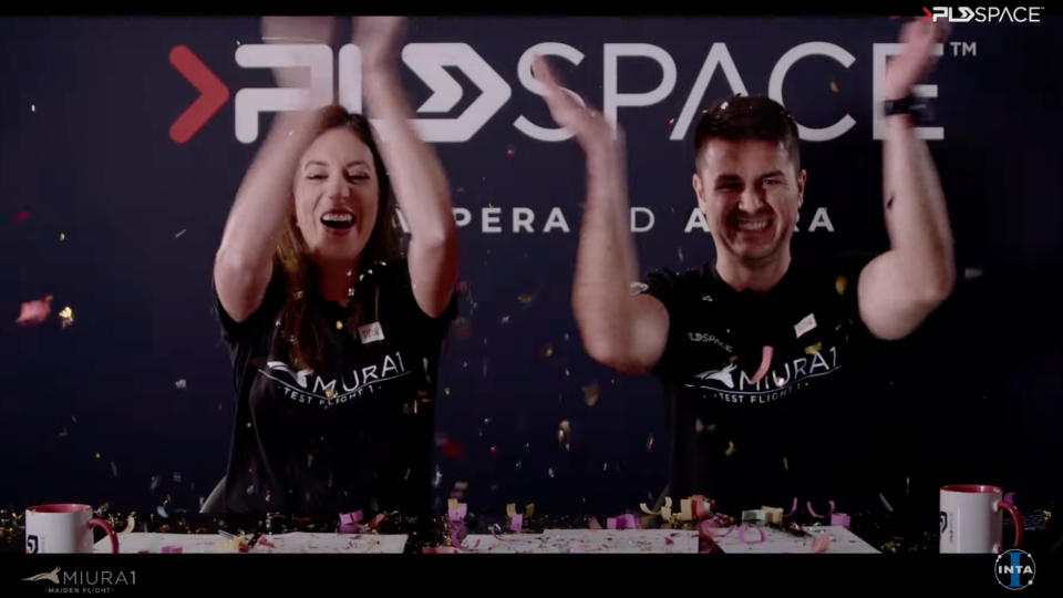a man and a woman in black t-shirts clap while confetti falls around them.