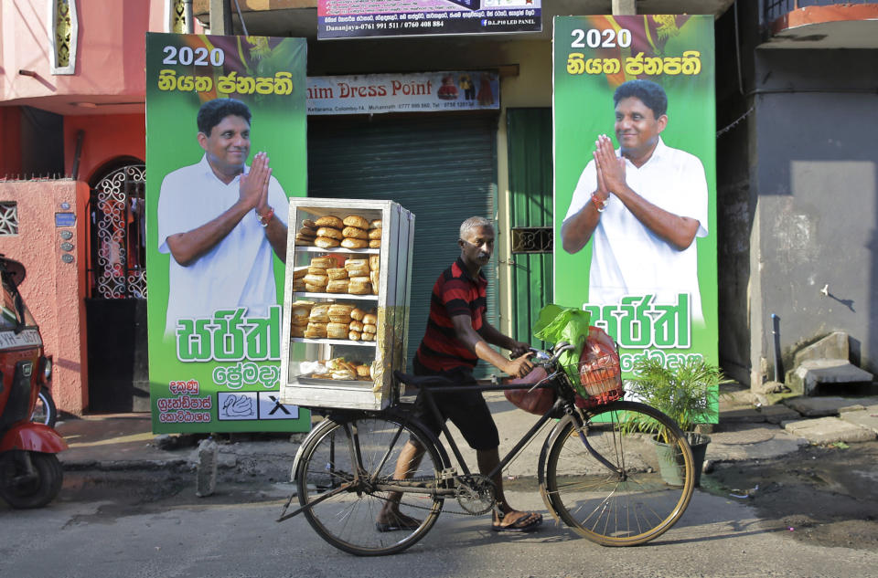 In this Wednesday, Nov. 13, 2019 photo, a Sri Lankan bread vendor pushes his bicycle past election propaganda of presidential candidate representing the governing party Sajith Premadasa in Colombo, Sri Lanka,. Sinhalese reads," 2020 definite president Sajith" Sri Lankans will be voting Saturday, Nov. 16, for a new president after weeks of campaigning that largely focused on national security and religious extremism in the backdrop of the deadly Islamic State-inspired suicide bomb attacks on Easter Sunday. (AP Photo/Eranga Jayawardena)