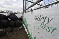 A construction fence featuring the words "Safety First" with a backdrop of the Olympic rings floating in the water in the Odaiba section Thursday, April 8, 2021, in Tokyo. The Tokyo Olympics are getting closer and things are starting to stir around the venues, though not as much as you might expect. Many preparations are still up in the air as organizers try to figure out how to hold the postponed games in the middle of a pandemic. (AP Photo/Eugene Hoshiko)