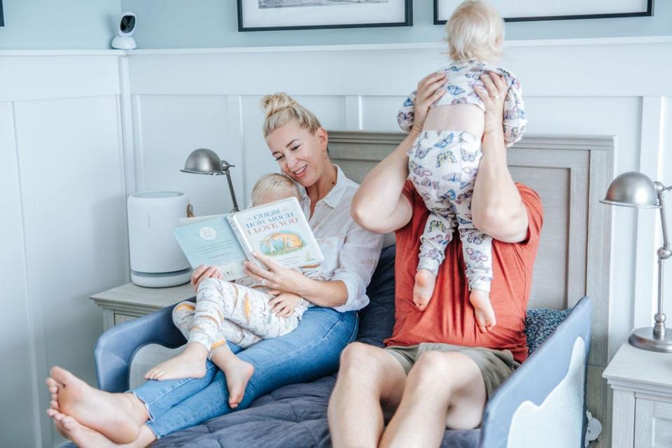 Christine Landis reading a book to her kids at bedtime. Her husband is sitting next to her and picking up one of her kids.