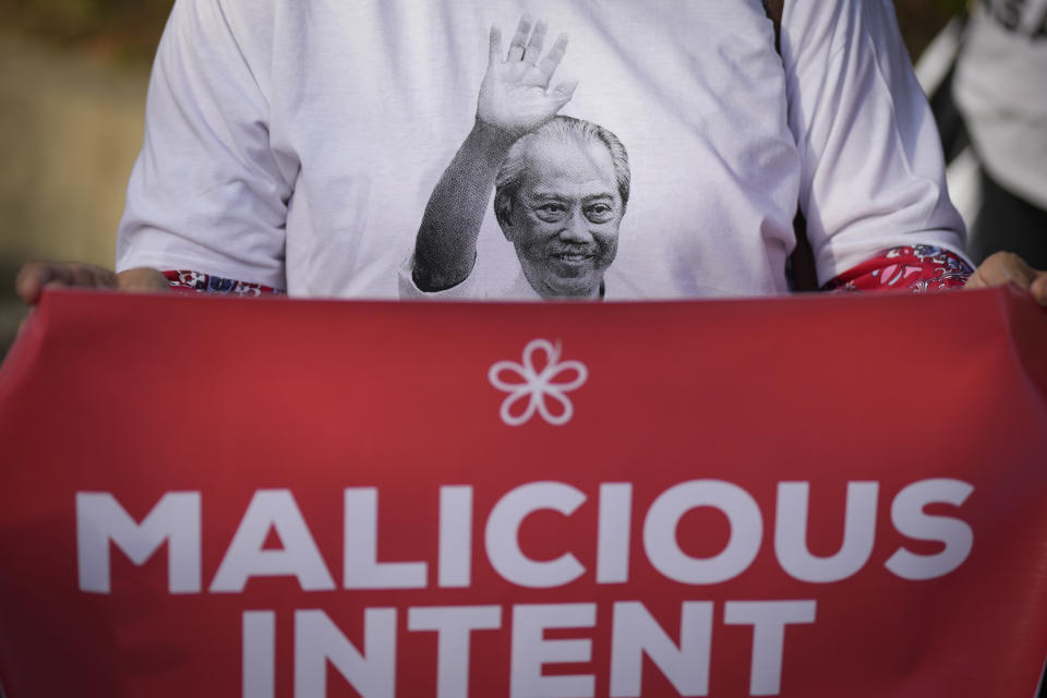 A supporter holds a poster and wears a T-shirt with Malaysia's former Prime Minister Muhyiddin Yassin picture to show support outside courthouse during a corruption charges in Kuala Lumpur, Malaysia, Friday, March 10, 2023. Muhyiddin, who led Malaysia from March 2020 until August 2021, will be the country's second leader to be indicted after leaving office. (AP Photo/Vincent Thian)