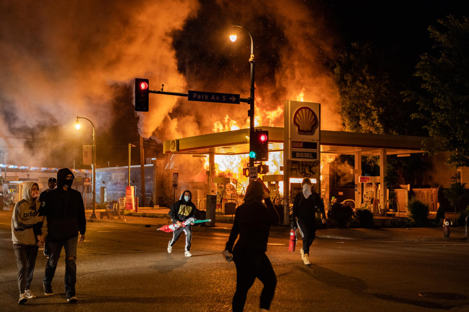 MINNEAPOLIS, MN - MAY 29: Protesters walk past a gas station on the corner of Park Ave S and E. Lake St that is on fire on Friday, May 29, 2020, in Minneapolis, MN. Protests in the wake of the death of George Floyd while in police custody swept country overnight Thursday.  (Photo by Salwan Georges/The Washington Post via Getty Images)