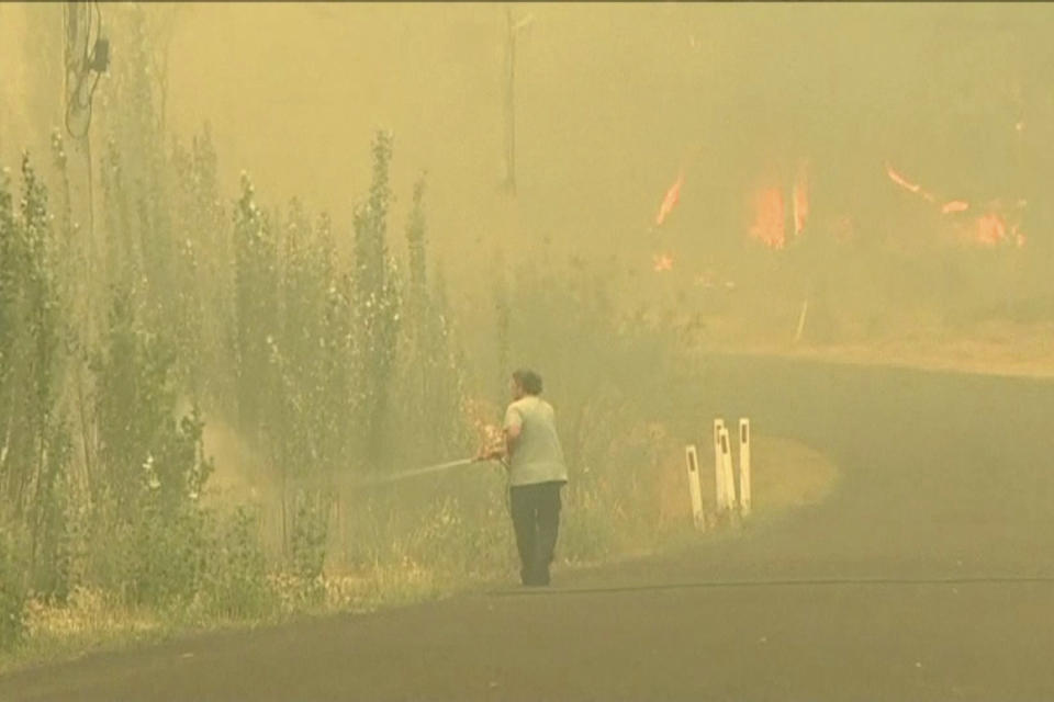 In this image made from video taken Dec. 21, 2019, a man sprays water on a fire in Lithgow, New South Wales state, Australia. Australian Prime Minister Scott Morrison on Sunday apologized for taking a family vacation in Hawaii as deadly bushfires raged across several states, destroying homes and claiming the lives of two volunteer firefighters.(Australian Broadcasting Corporation via AP)