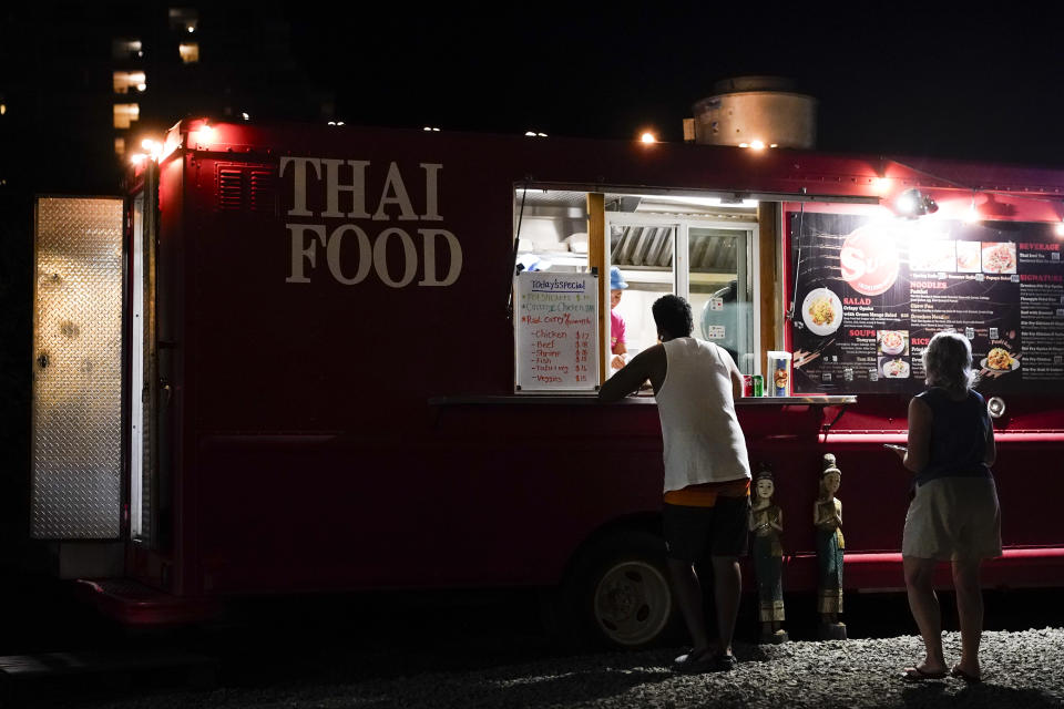 Visitors order from a truck at the Honoapiilani Food Truck Park, Thursday, Dec. 7, 2023, in the beach resort community of Kaanapali in Lahaina, Hawaii. Residents and survivors still dealing with the aftermath of the August wildfires in Lahaina have mixed feelings as tourists begin to return to the west side of Maui. (AP Photo/Lindsey Wasson)
