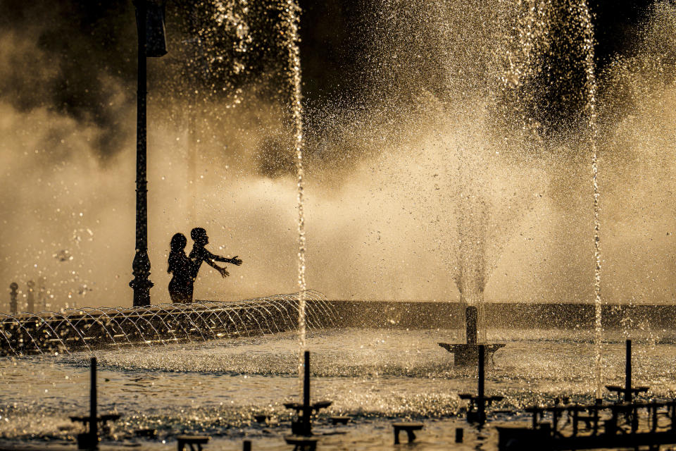 Children enjoy the drizzle from a public fountain before sunset in Bucharest, Romania, Thursday, June 20, 2024 as temperatures exceeded 38 degrees Celsius (100.4 Fahrenheit). The national weather forecaster issued a orange warning for western and southern Romania where temperatures are expected to reach 38 degrees Celsius (100.4 Fahrenheit) in the coming days. (AP Photo/Vadim Ghirda)