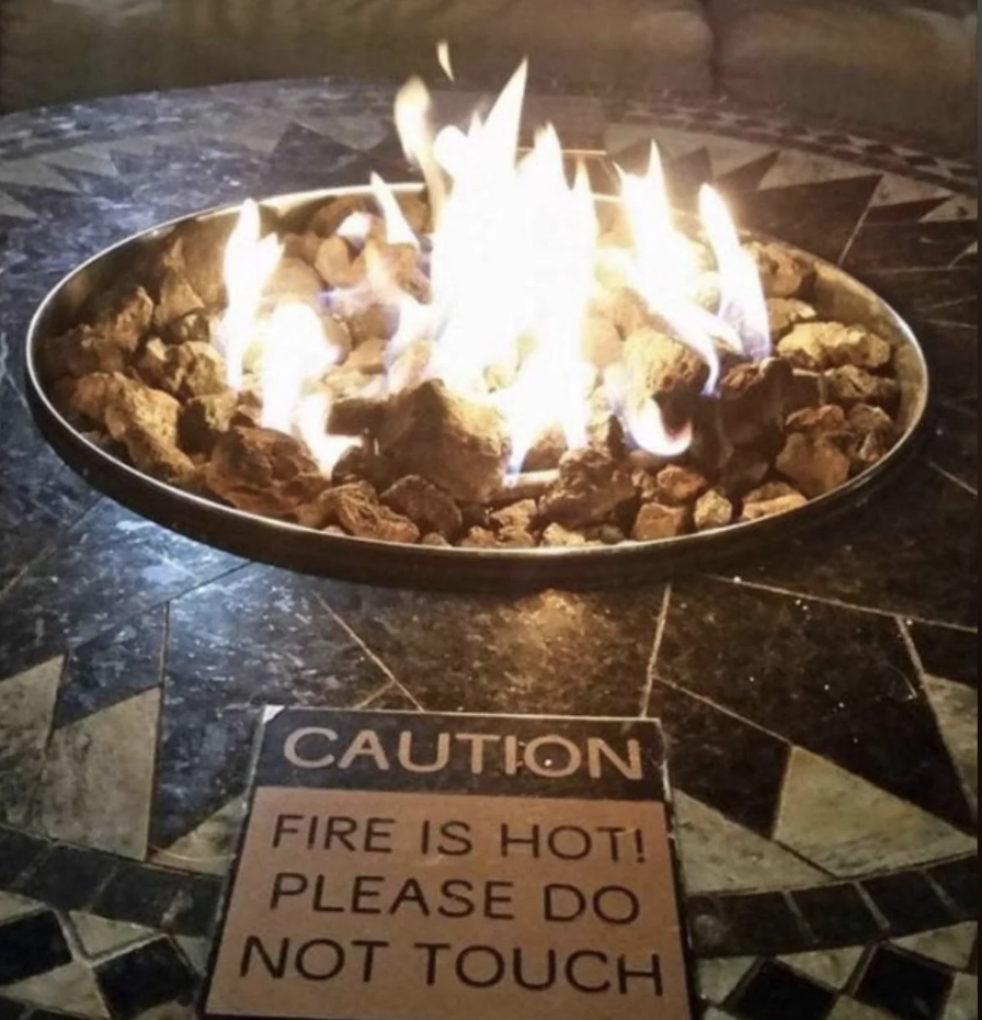 A fire pit with flames and a caution sign reading "FIRE IS HOT! PLEASE DO NOT TOUCH"
