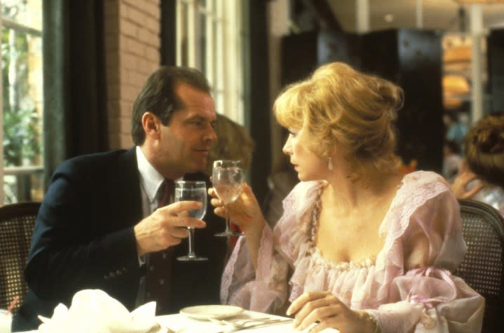 A man raises his glass for cheers with a woman while sitting at a table.