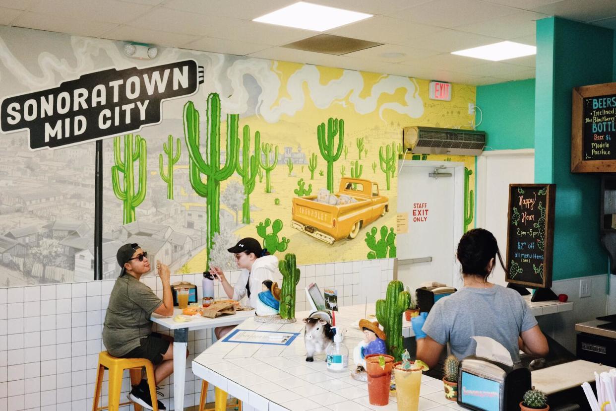 Two guests dine against an interior wall of Sonoratown Cantina with a mural of cactus and a truck carrying masa