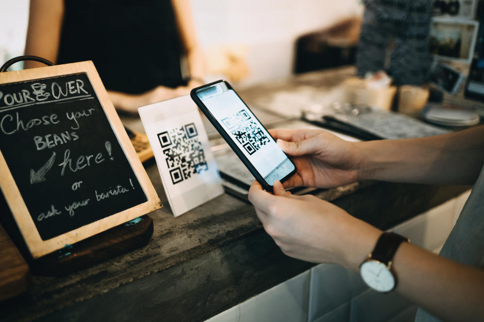 Customer scanning QR code, making a quick and easy contactless payment with her smartphone in a cafe