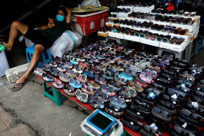 A glasses vendor wearing a protective mask uses a smartphone while waiting for the customers at Tanah Abang textile market, as the outbreak of coronavirus disease (COVID-19) continues in Jakarta