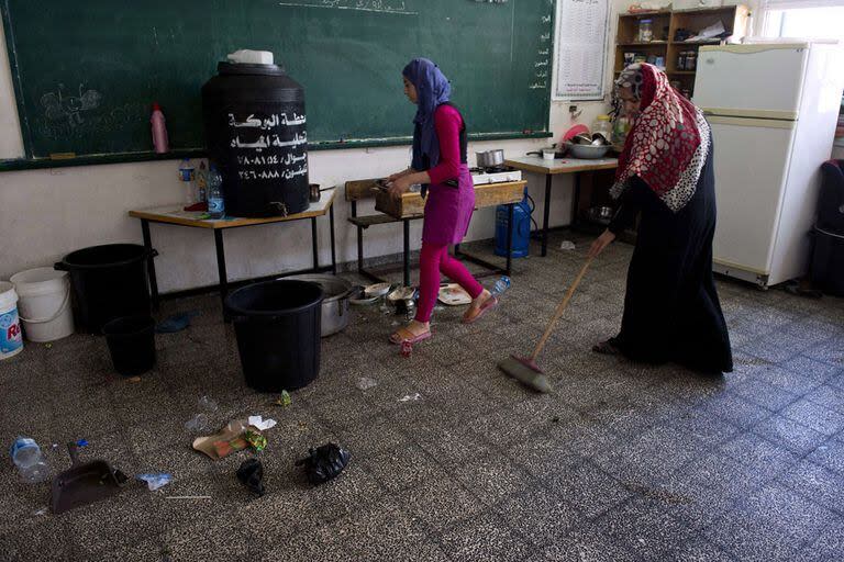 Dos mujeres palestinas que viven junto a 20 familiares en una escuela de Naciones Unidas en Jabalia, en el norte de Gaza, limpian el aula que hace de cuarto