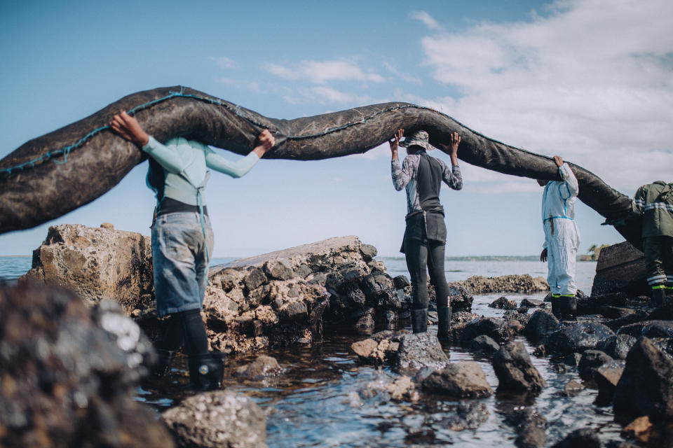 Volunteers lift part of a natural boom made of sugarcane leaves onto their shoulders in Bois des Amourettes, Mauritius on Wednesday. The boom was then hauled into a boat, to be placed into the lagoon. (Beata Albert)