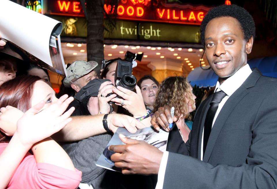 Edi Gathegi in a suit signing autographs