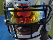 Carolina Panthers coach Ron Rivera, left, and the team are reflected in DeAngelo William's helmet during an NFL football practice at NFL football training camp in Spartanburg, S.C., Saturday, July 26, 2014. (AP Photo/Chuck Burton)