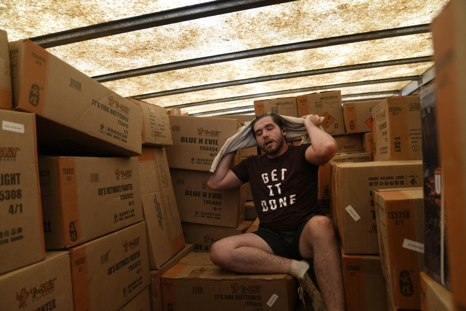 Ethan Hickman uses a towel to wipe off sweat while sorting boxes of fireworks inside a stiflingly hot trailer at Powder Monkey Fireworks ahead of the opening of the stand Monday, June 17, 2024, in Weldon Spring, Mo. (AP Photo/Jeff Roberson)