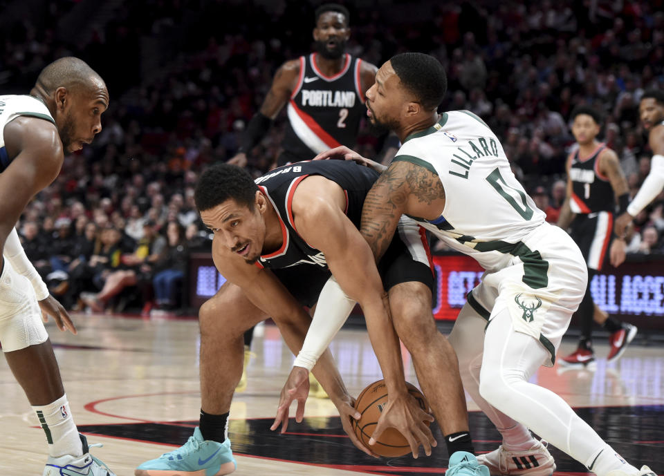 Milwaukee Bucks guard Damian Lillard (0) reaches in on Portland Trail Blazers guard Malcolm Brogdon, center, as forward Khris Middleton, left, looks on during the first half of an NBA basketball game in Portland, Ore., Wednesday, Jan. 31, 2024. (AP Photo/Steve Dykes)