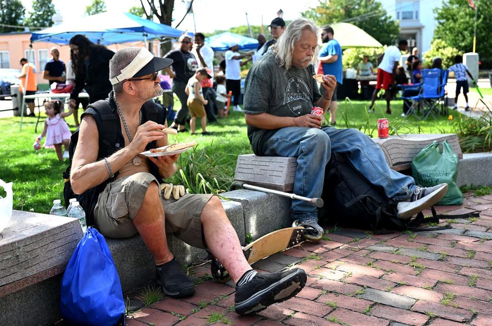 Stanley Galazka, left, and Troy Hatfield, both of Framingham and in insecure housing situations, enjoy free pizza at the Framingham Downtown Common, Sept. 3, 2022. The event also included care packages and was the brainchild of Cheniel Garcia, an aspiring hip-hop artist who turned his life around after spending time in prison.