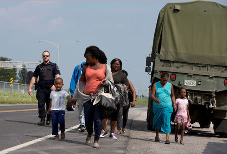 A group of asylum seekers walk down the street as they are escorted from their tent encampment to be processed at Canada Border Services in Lacolle, Quebec, Canada August 11, 2017. REUTERS/Christinne Muschi