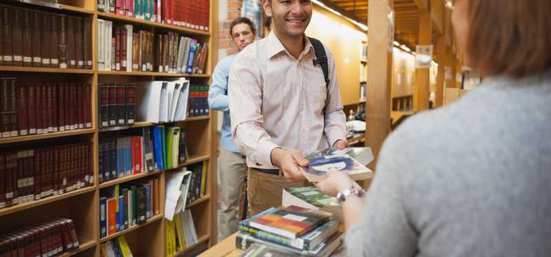 Young man checking out a book at the library.