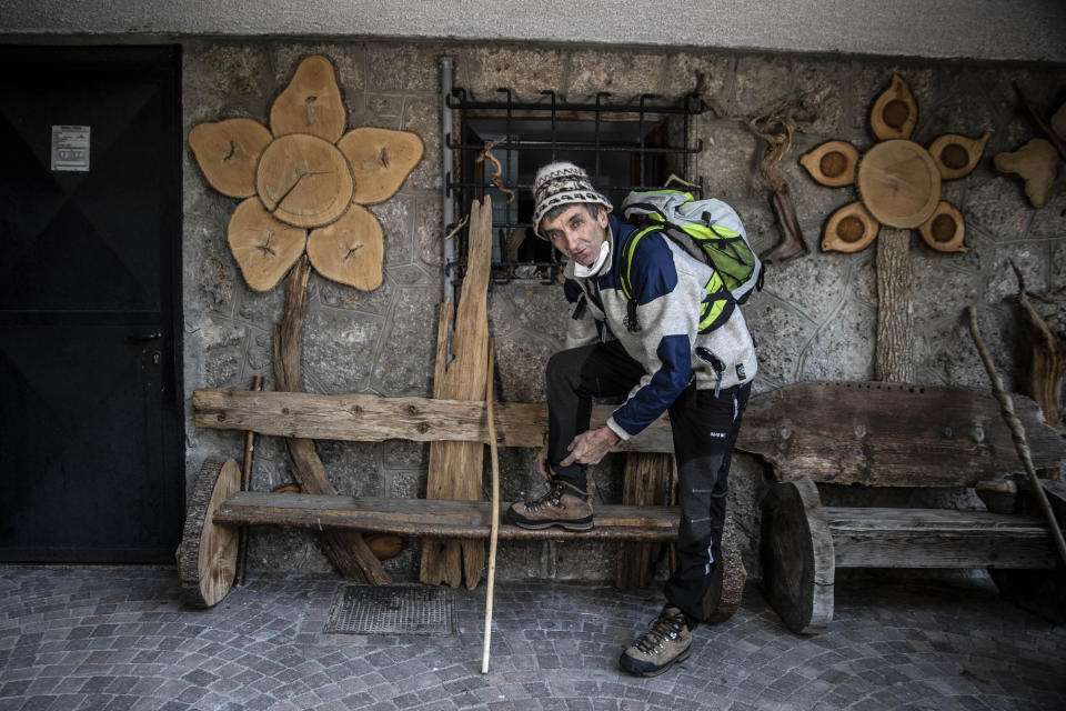 In this image taken on Thursday, April 23, 2020, alpine guide Ernesto Cocchetti, 57, puts on his hiking boots as he prepares to go walking, in Castione Della Presolana, near Bergamo, northern Italy. Cocchetti predicts a return to "living with nature's rhythms" once government restrictions to prevent the spread of COVID-19 will be eased. (AP Photo/Luca Bruno)