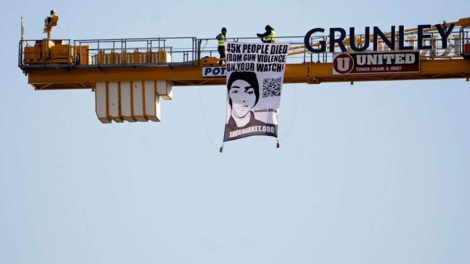 Manuel Oliver despliega un cartel con la cara de su hijo desde una enorme grúa de construcción. Washington, febrero 14, 2022.