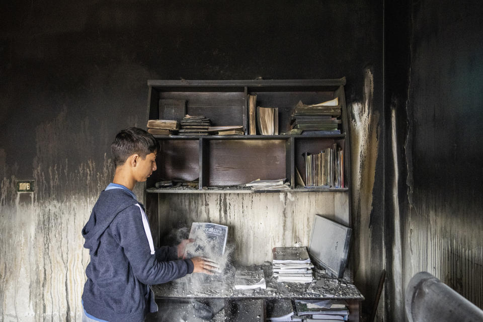 Ali Fawaz checks destroyed books and notebooks inside his damaged family house that was hit by Israeli shelling in the Kfar Kila border village with Israel in south Lebanon, Saturday, Nov. 25, 2023. With a cautious calm prevailing over the border area in south Lebanon Saturday, the second day of a four-day cease-fire between Hamas and Israel, villages that had emptied of their residents came back to life at least briefly. (AP Photo/Hassan Ammar)