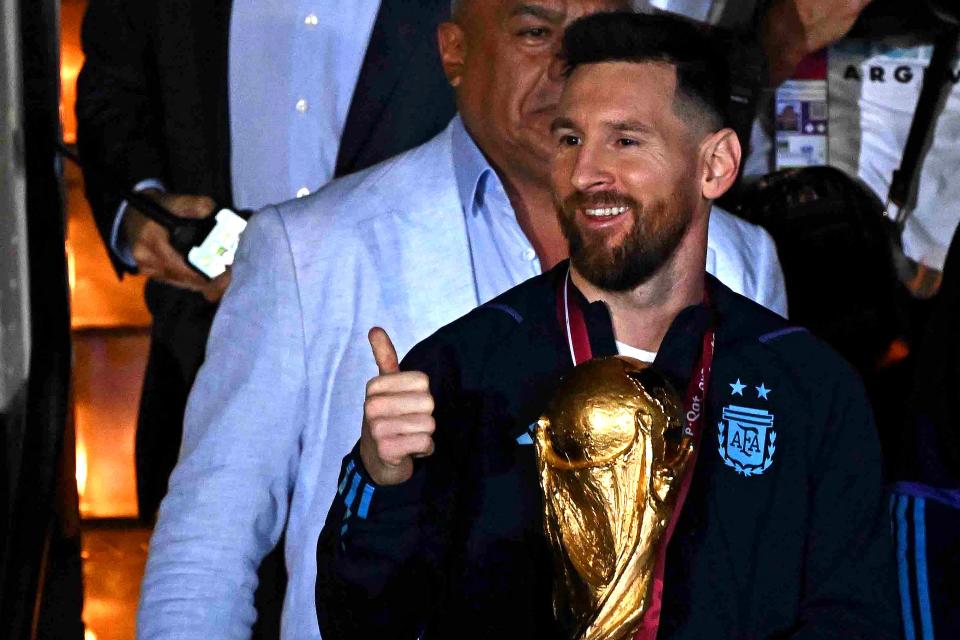 Argentina's captain and forward Lionel Messi (C) holds the FIFA World Cup Trophy alongside Argentina's coach Lionel Scaloni (R) upon arrival at Ezeiza International Airport after winning the Qatar 2022 World Cup tournament in Ezeiza, Buenos Aires province, Argentina on December 20, 2022. (Photo by Luis ROBAYO / AFP) (Photo by LUIS ROBAYO/AFP via Getty Images)