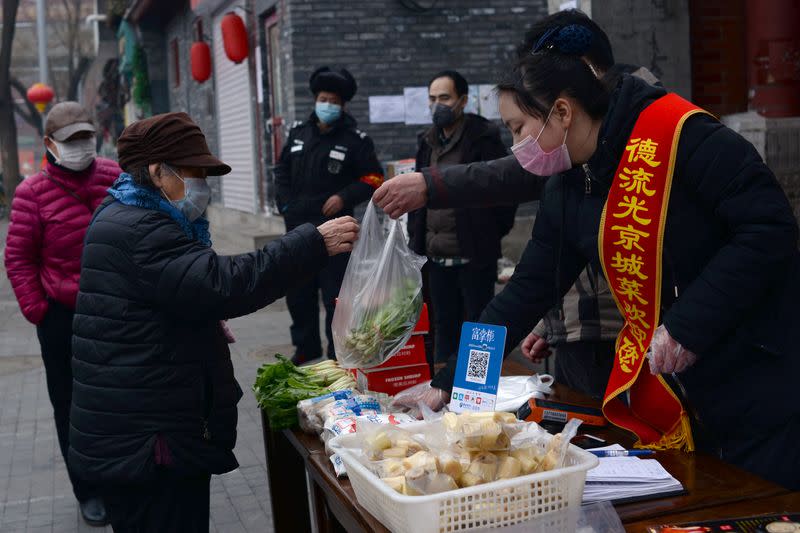 Woman wearing a face mask buys vegetables from a stall set up by a restaurant outside its outlet